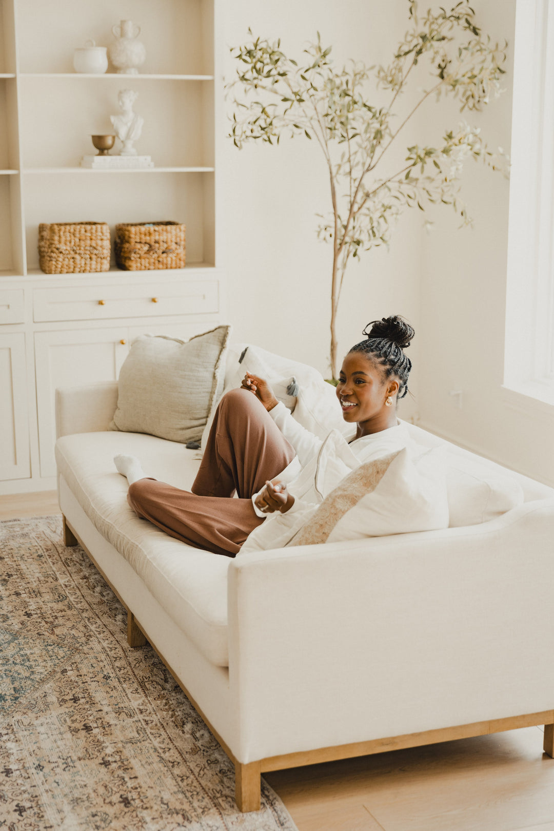 A young mom lounges in a cozy sofa chair, relaxed and smiling. Natural light warms the space.